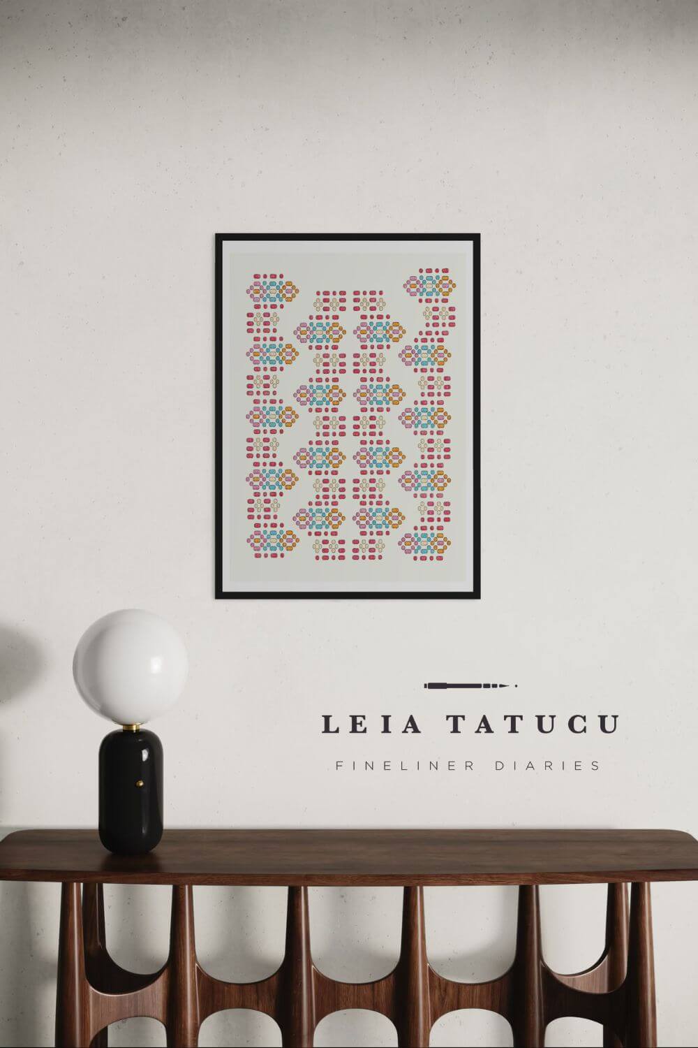 Geometric motif pattern art print in a black frame hanging above a modern wooden table with a lamp.